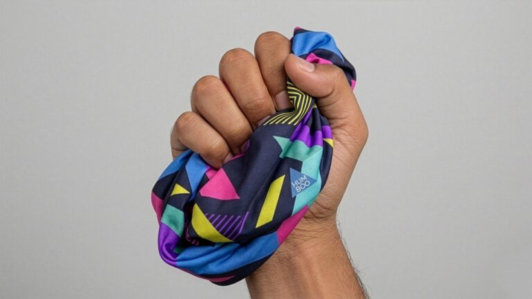 Dłoń trzyma zwinięty komin wielofunkcyjny Humboo — ultralekki, kompaktowy format do magazynu i transportu.