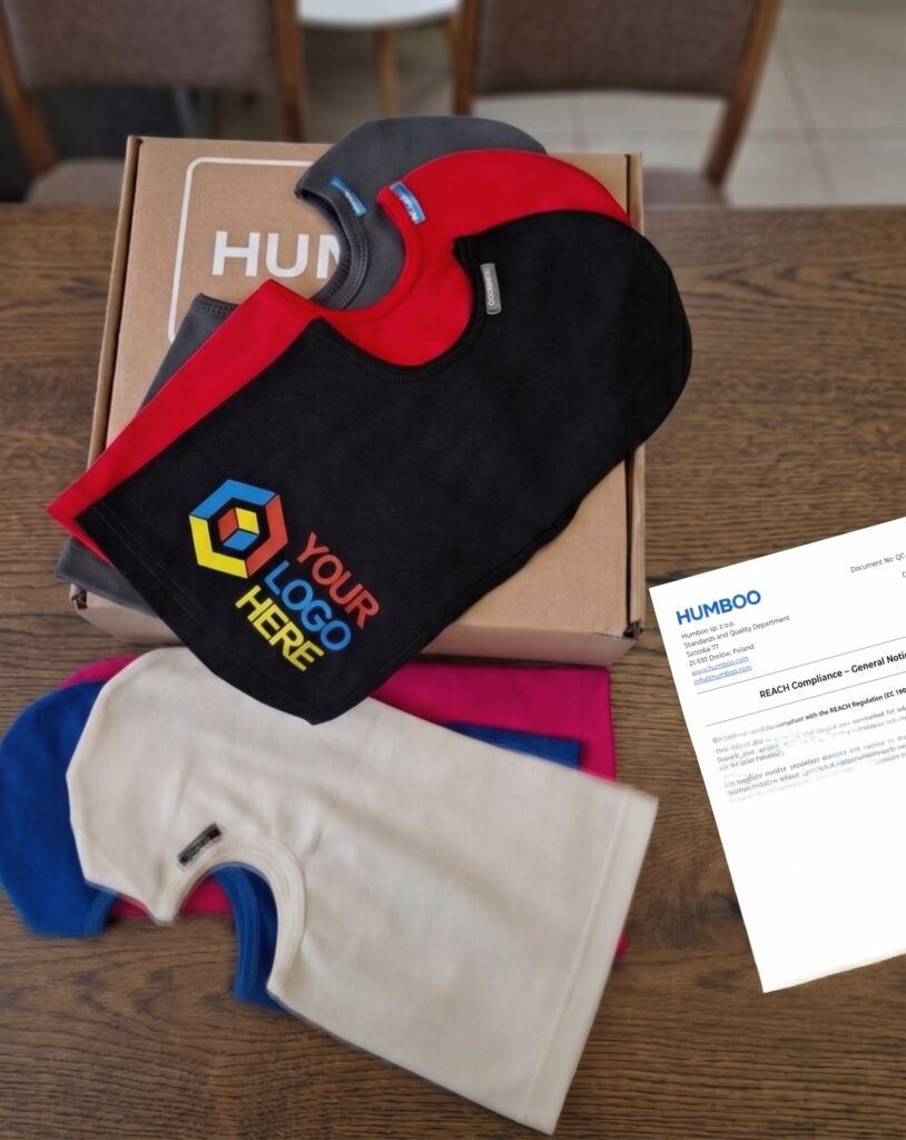 Kominiarki bawełniane w kilku kolorach z nadrukiem logo, ułożone na kartonie Humboo obok dokumentu zgodności REACH